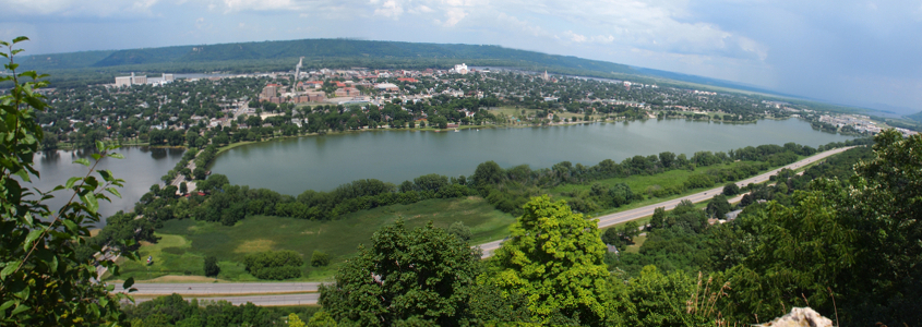 [Approximately 4 photos stitched together presenting a curved panoramic view of the lake and the road at the lower edge of the bluff and the city on the far side of the lake.]